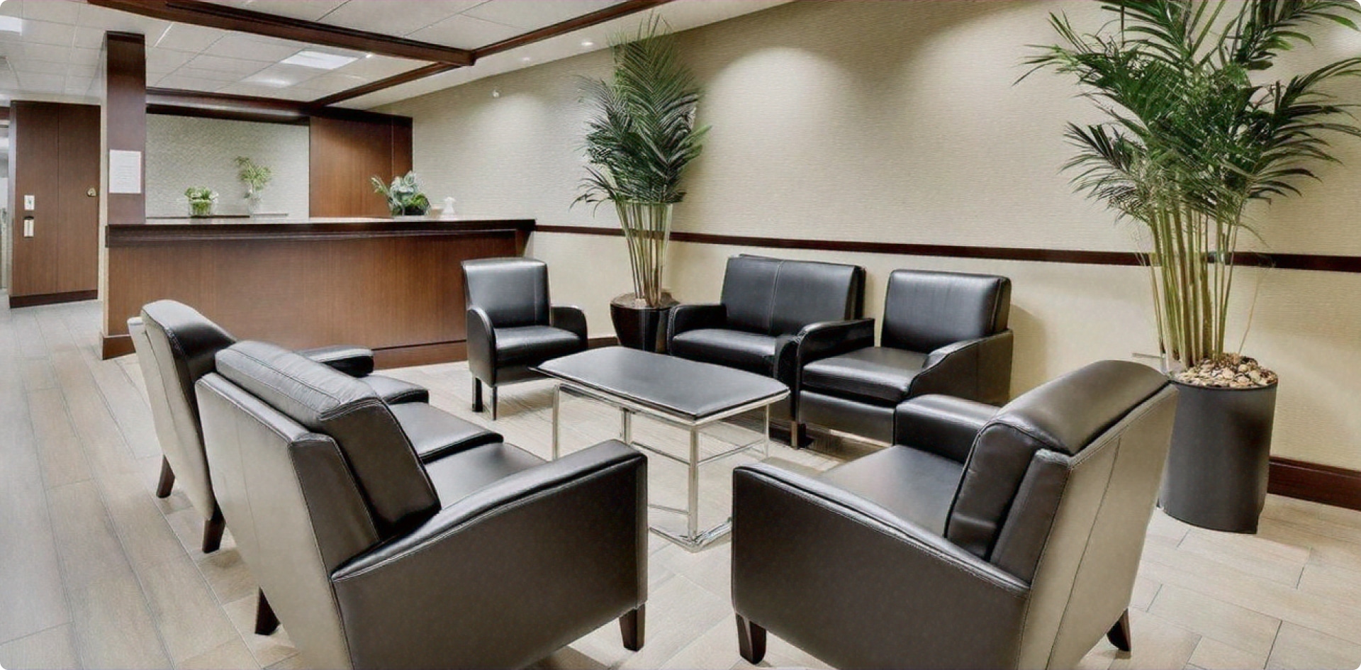 Modern office waiting room with black leather chairs, small table, potted plants, and wooden reception desk. Neutral color palette creates a calm atmosphere.